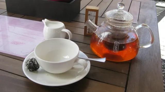 A glass teapot of amber tea sits beside a white cup.