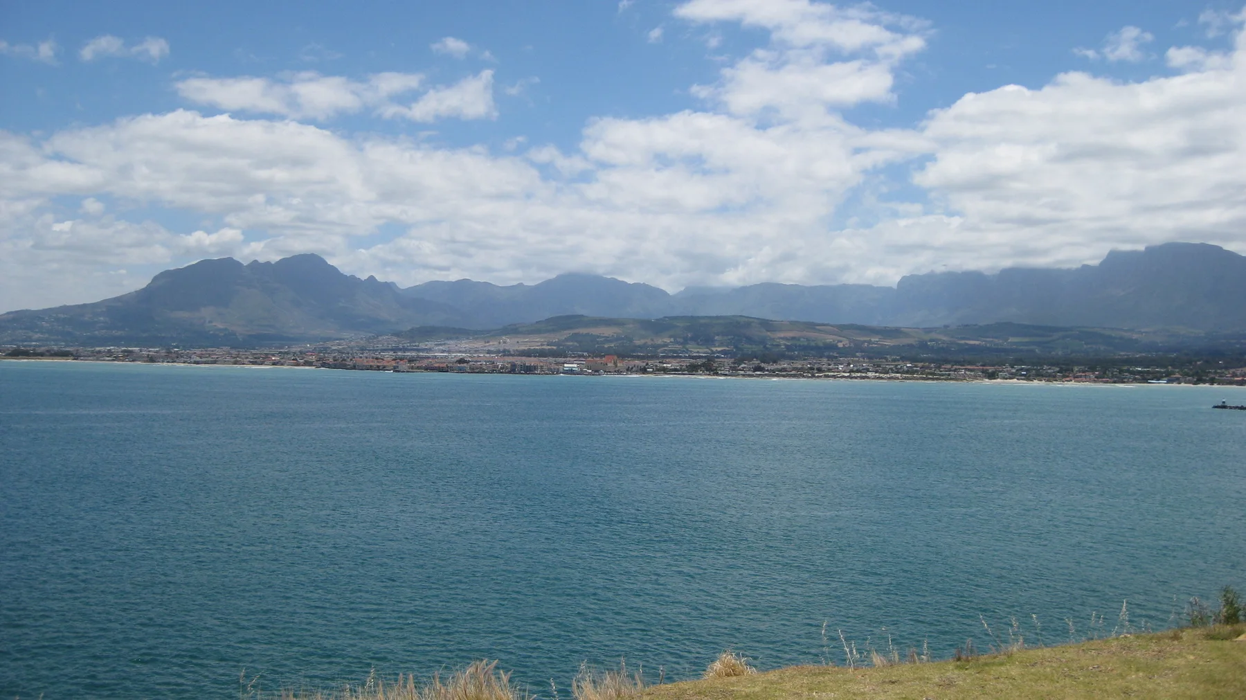 Blue bay water lies below distant mountains and scattered clouds.