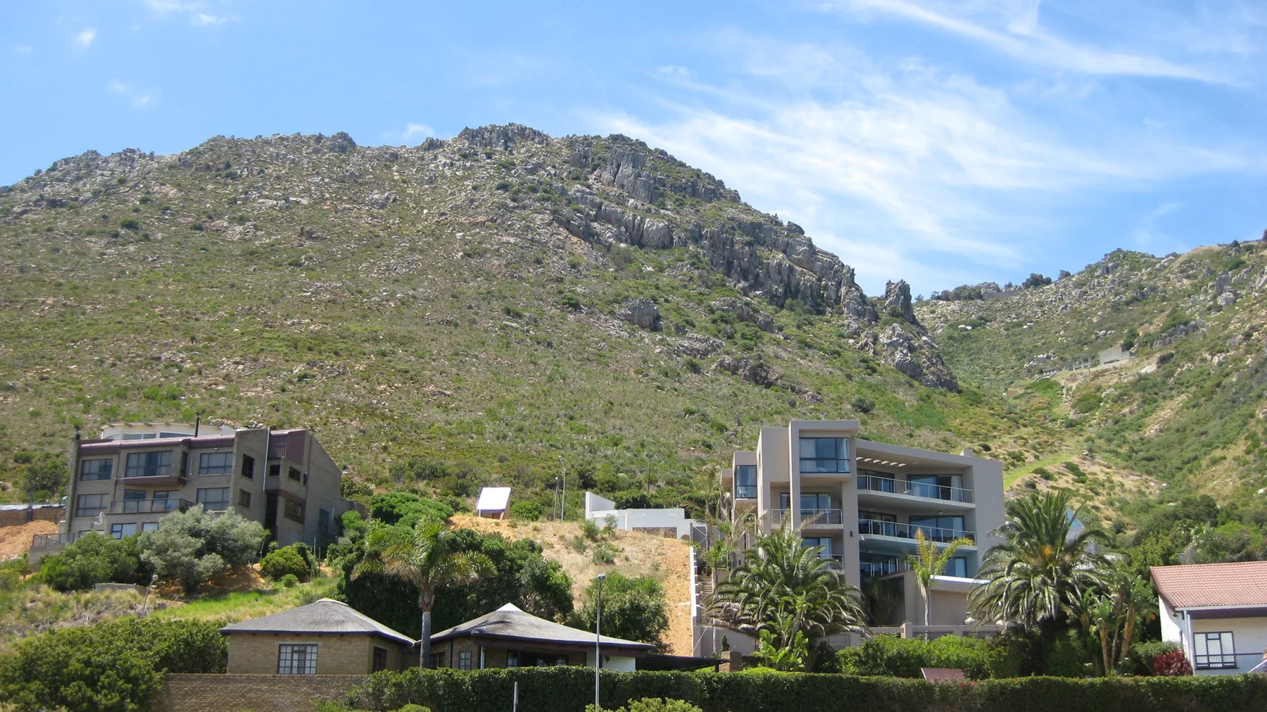 Modern homes sit below a rocky hilltop crest.