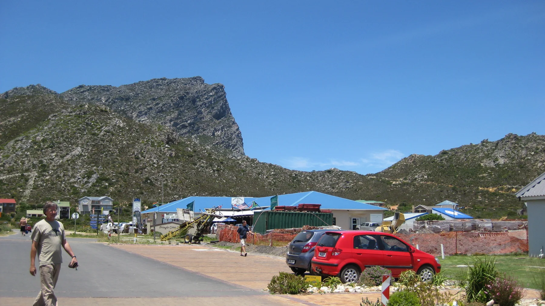 Roadside stalls and parked cars sit below a steep rocky peak.