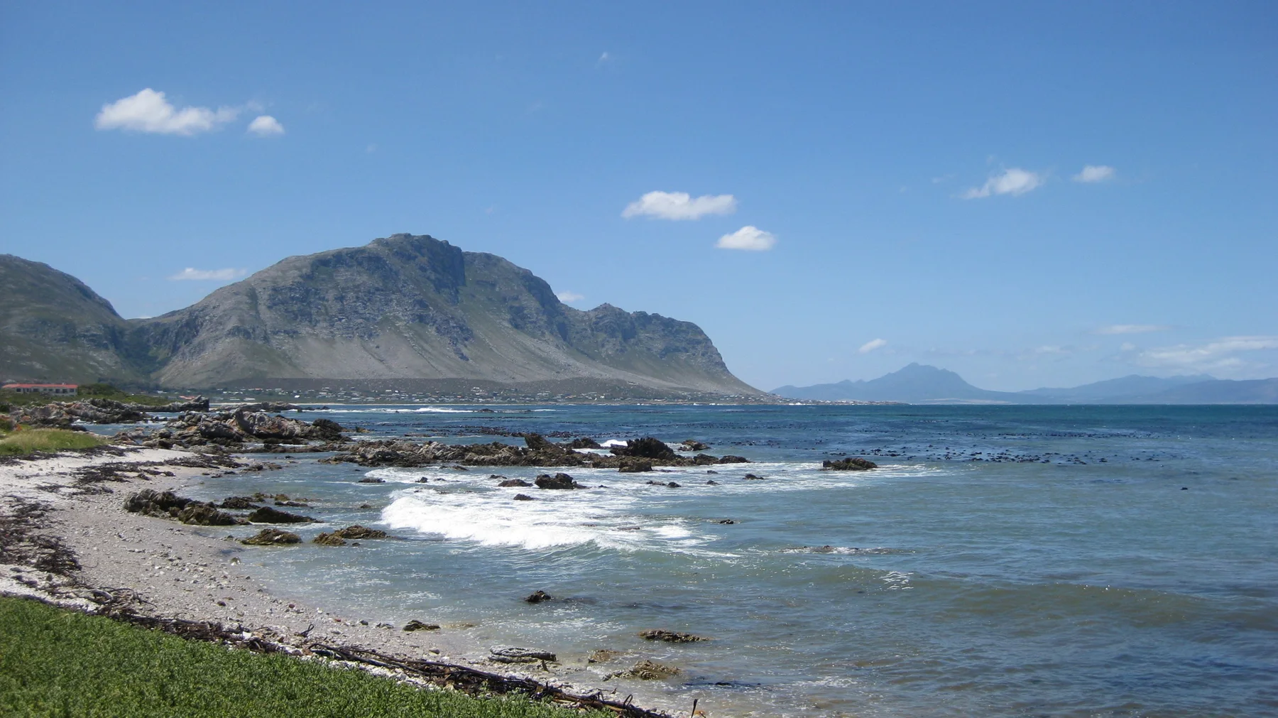 Waves cross a rocky bay beneath a rugged mountain range.
