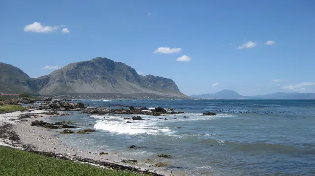Waves cross a rocky bay beneath a rugged mountain range.