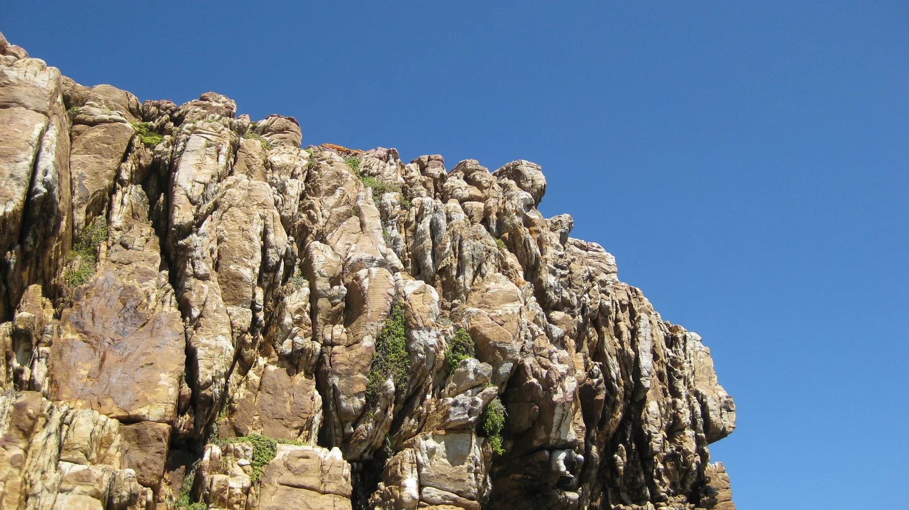 Sunlight warms a jagged golden rock face against blue sky.
