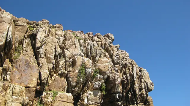 Sunlight warms a jagged golden rock face against blue sky.
