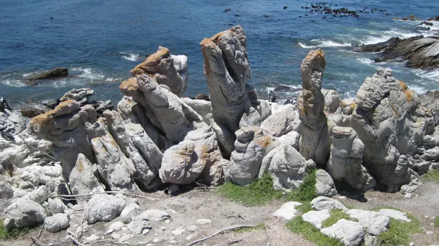 Tall pale rock spires rise above blue coastal water.