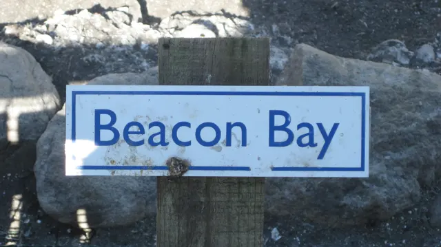 A small sign marked Beacon Bay is fixed to a wooden post.
