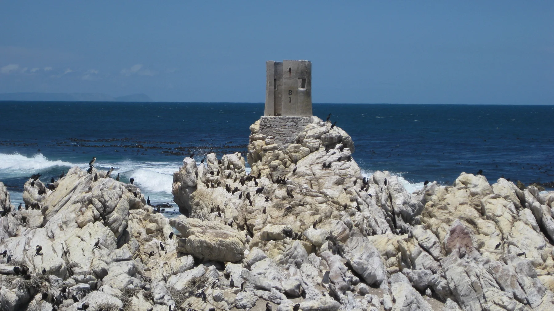A short cylindrical beacon stands atop pale coastal rocks.