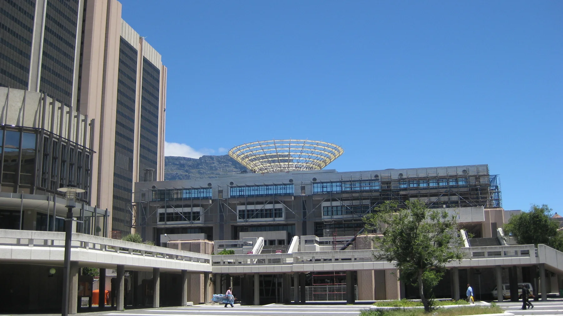 A modern building with a rooftop framework faces an open plaza.