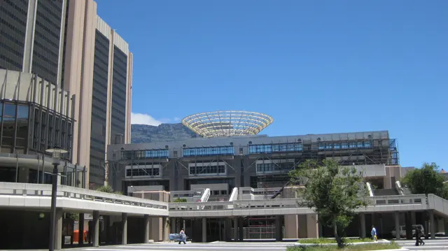 A modern building with a rooftop framework faces an open plaza.