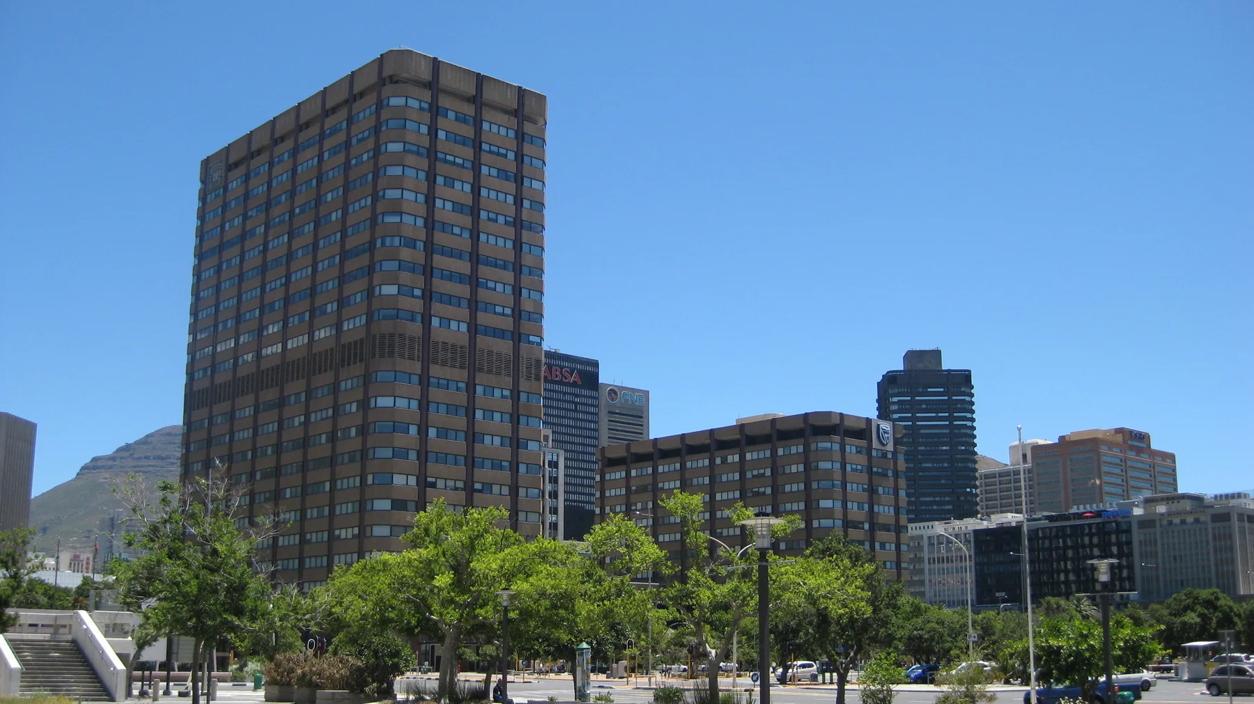 A tall rectangular windowed block rises above leafy street trees.