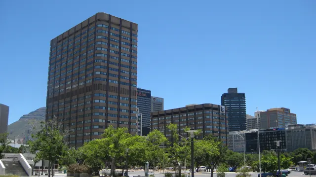 A tall rectangular windowed block rises above leafy street trees.