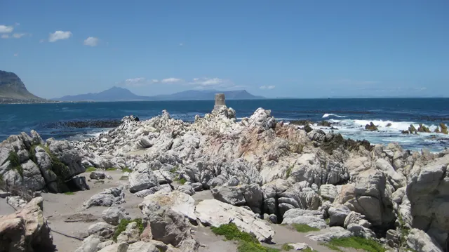 A small beacon appears beyond a field of pale coastal rocks.
