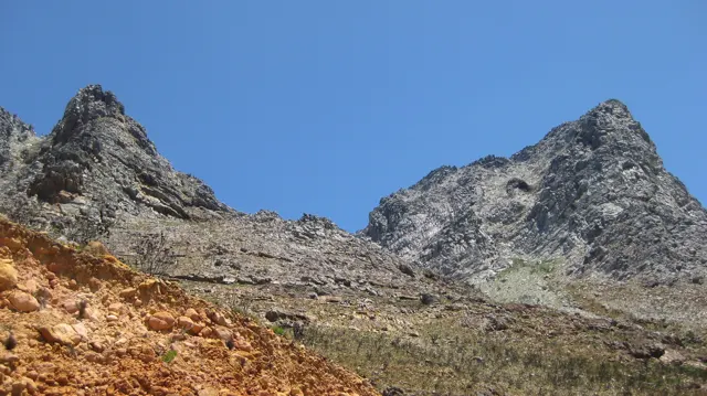 Two sharp rocky peaks rise above an ochre roadside cutting.