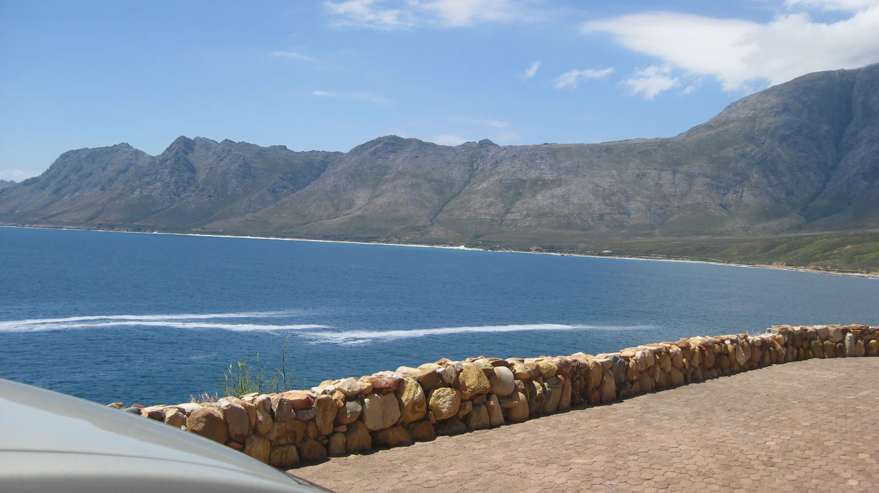A stone wall overlooks a deep blue bay and rugged mountains.