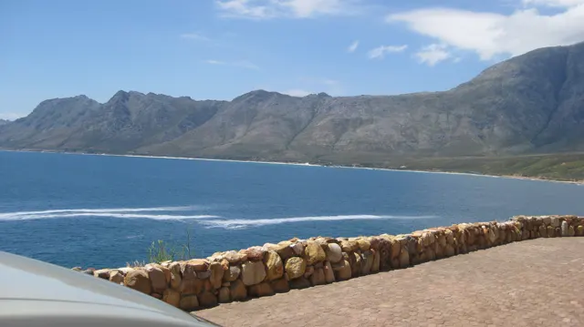 A stone wall overlooks a deep blue bay and rugged mountains.