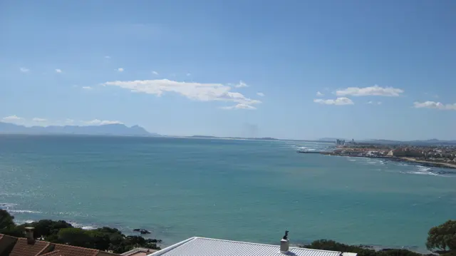 Foreground roofs overlook a broad quiet bay and distant mountains.