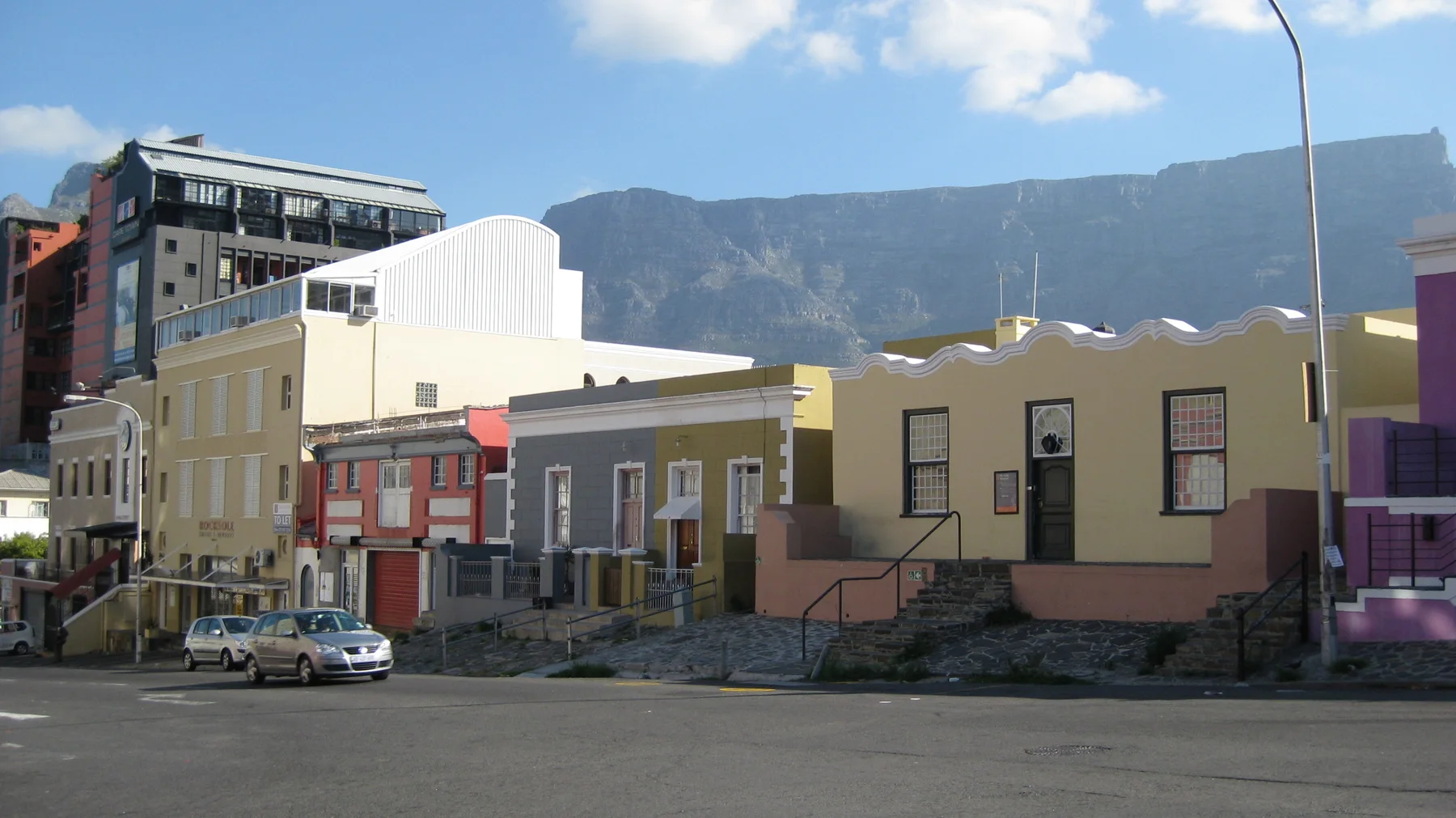 Pastel-colored houses line a street beneath a broad mountain.