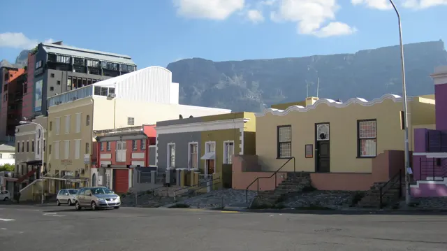 Pastel-colored houses line a street beneath a broad mountain.