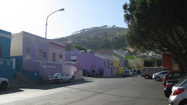 Purple and yellow houses line a sloping street with parked cars.