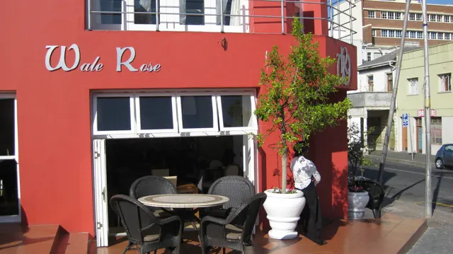 A red facade marked Wale Rose opens onto a small outdoor table.