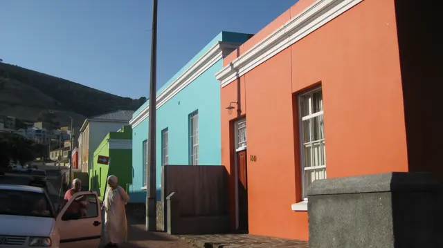 Orange and blue walls line a narrow sunlit pavement.