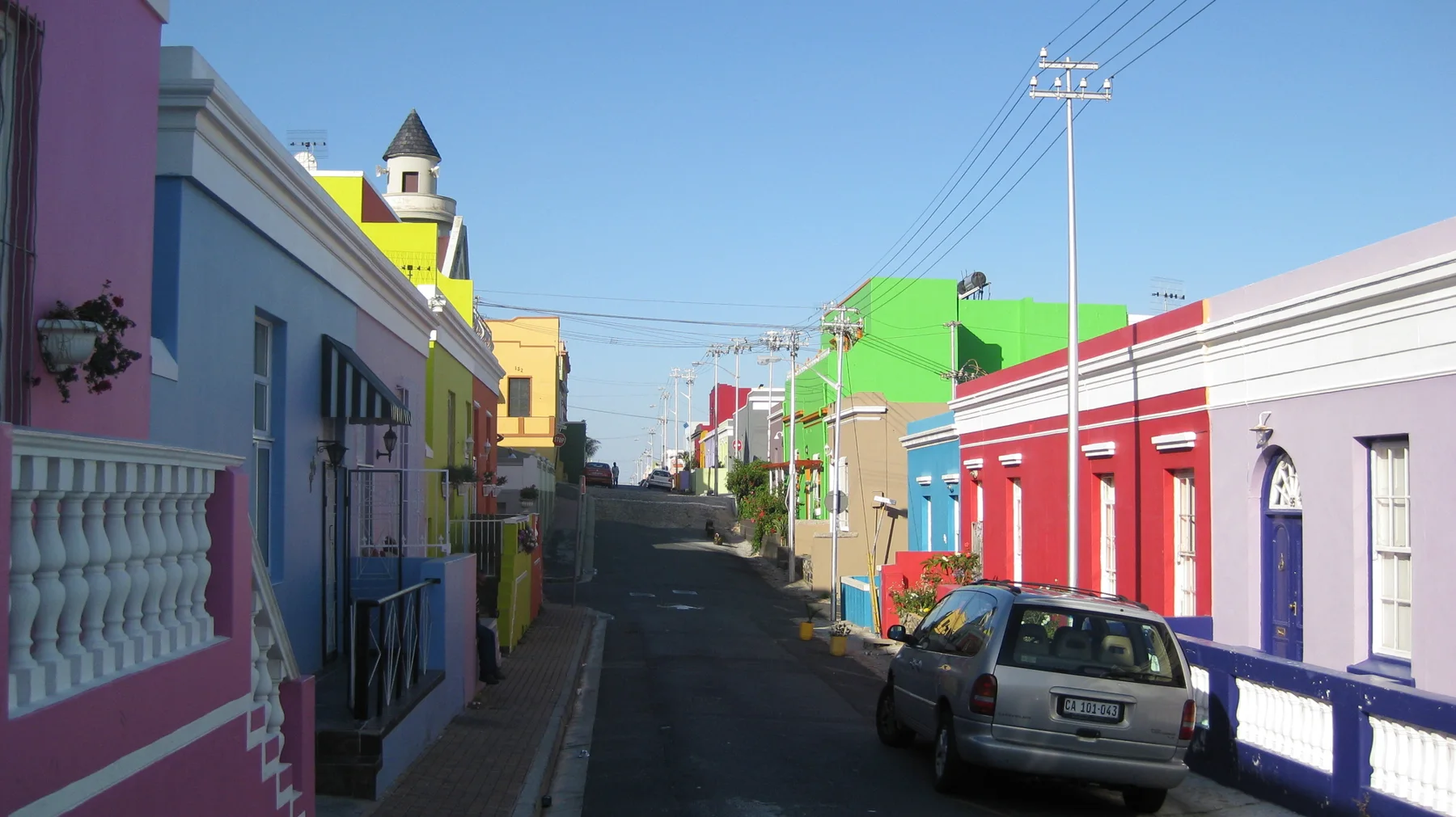 Vividly painted houses line a narrow street with parked cars.