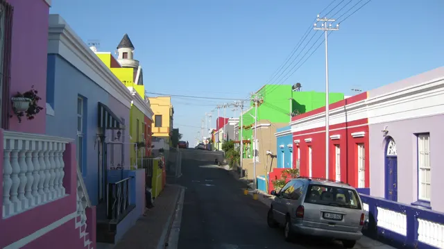Vividly painted houses line a narrow street with parked cars.