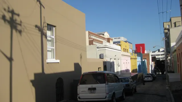 Utility shadows cross a pale facade beside parked cars.