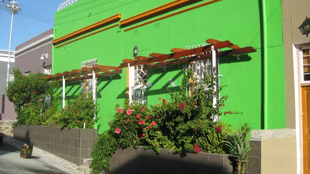 A bright green house has a flower-covered pergola above its front wall.