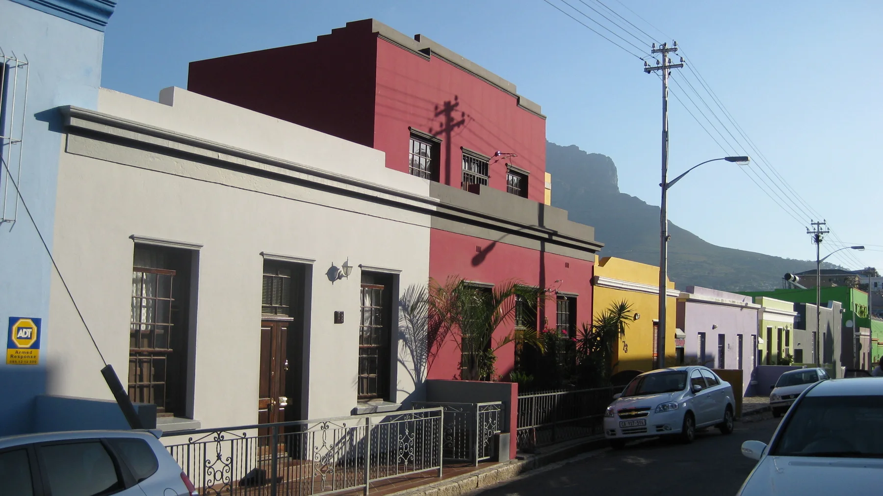 A cream house stands beside a taller red facade on a slope.