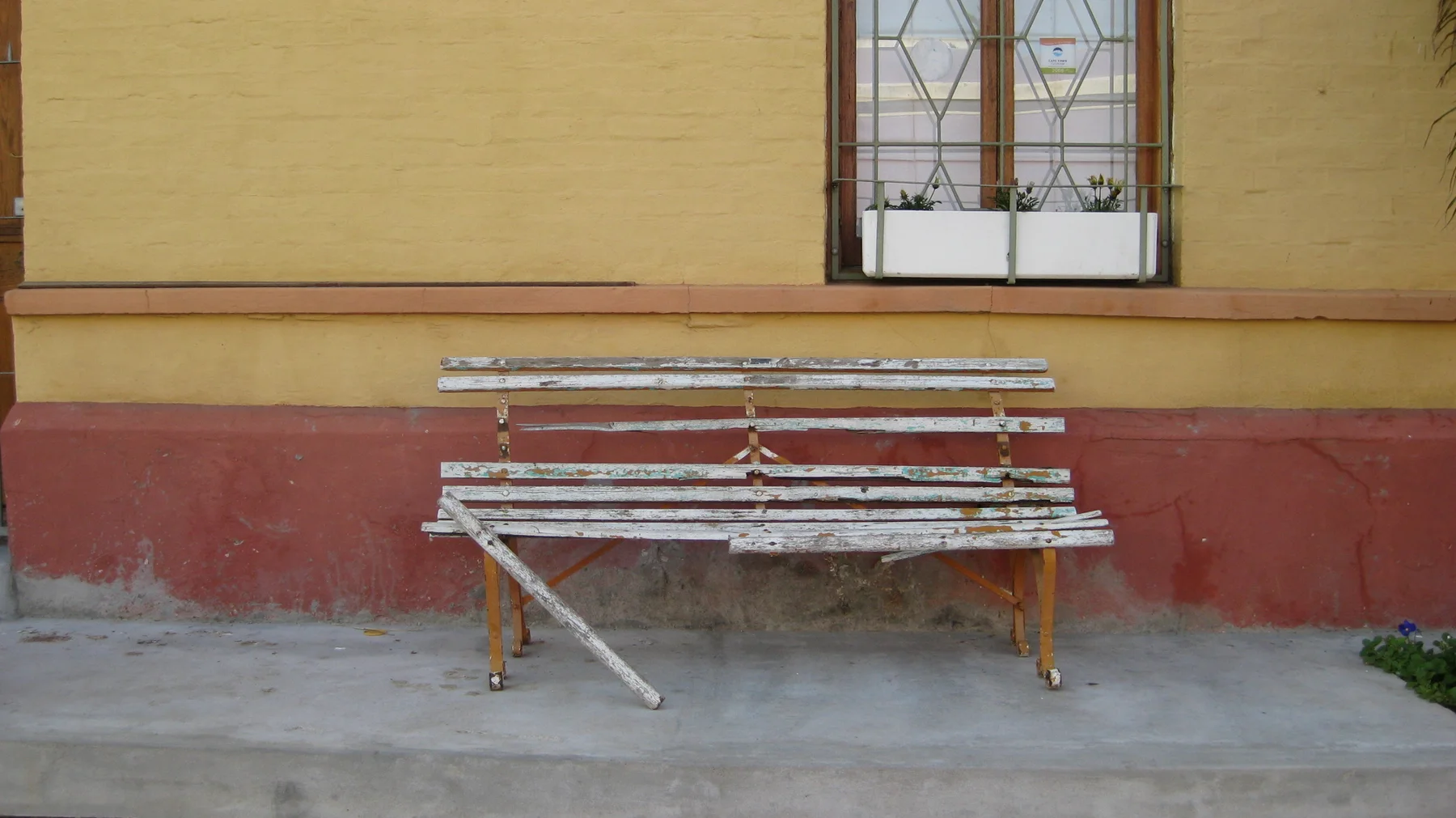A weathered slatted bench rests against an ochre and red wall.