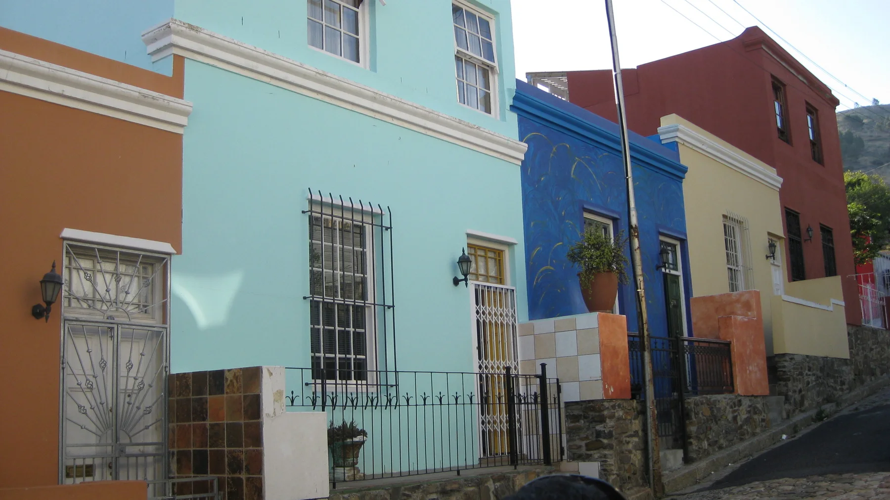 Turquoise, blue and cream facades line a narrow pavement.
