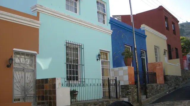 Turquoise, blue and cream facades line a narrow pavement.