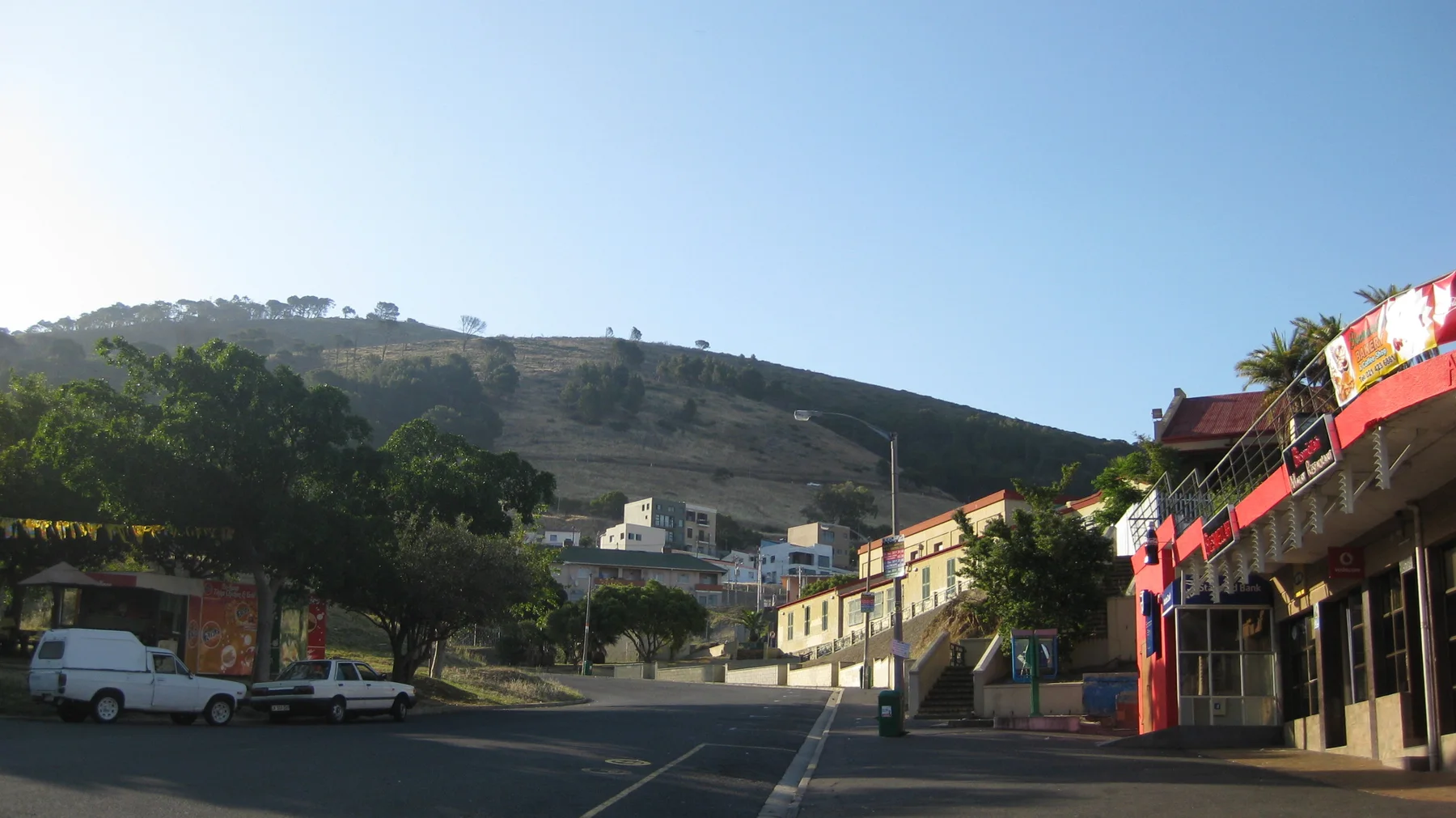 A broad junction lies beneath a low hill and roadside shops.