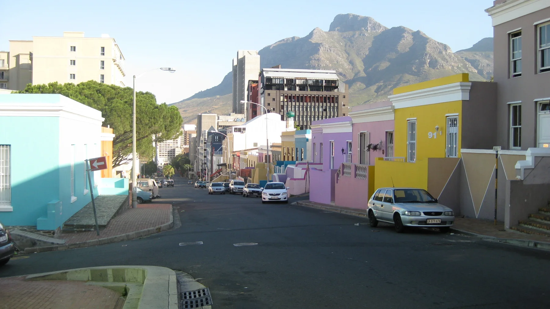 Pastel facades lead toward taller city buildings and a rocky mountain.