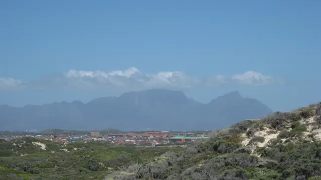 A hazy mountain range rises beyond low scrub and distant roofs.