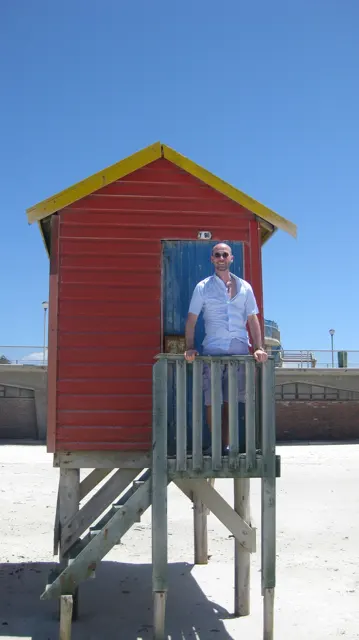 A person in white stands on the landing of a red hut with green steps.