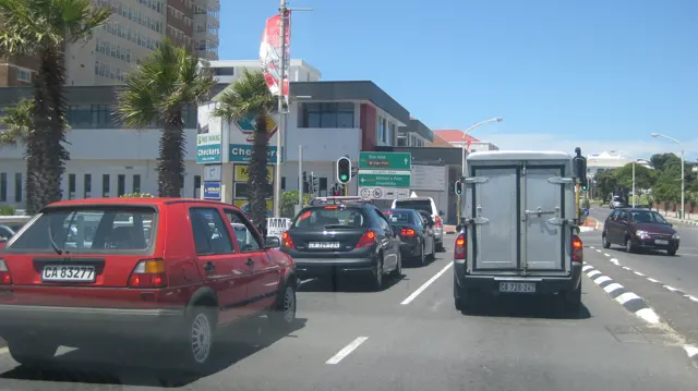 A van and several cars travel along a busy town street.