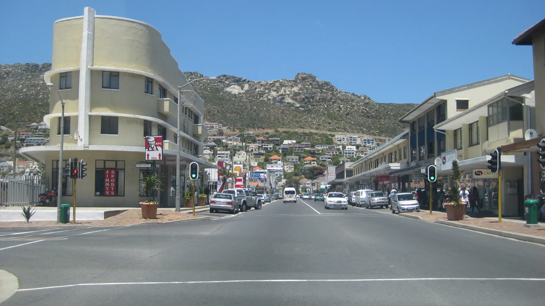 A pale yellow corner building overlooks an intersection beneath a hillside dotted with houses.
