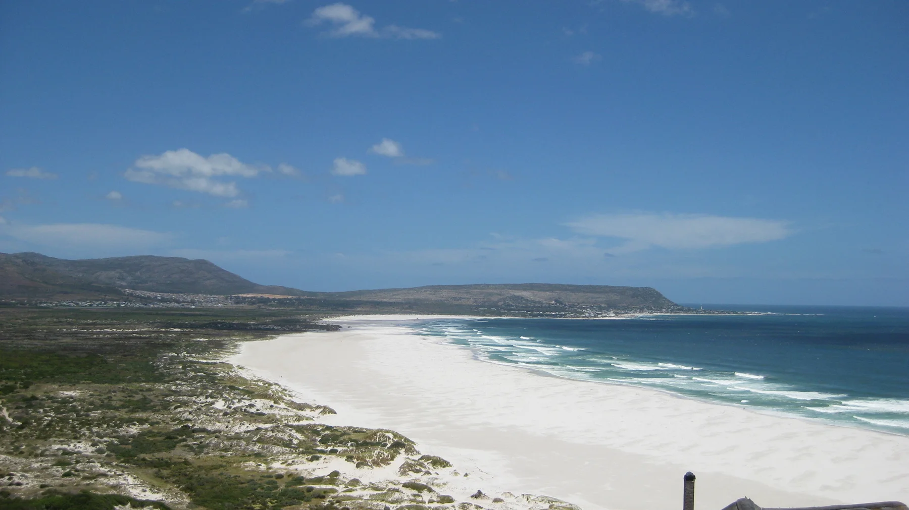 A sweeping white shoreline separates the blue sea from a broad belt of coastal vegetation.