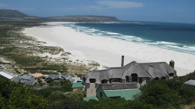 A thatched house appears below a viewpoint overlooking a long white beach.