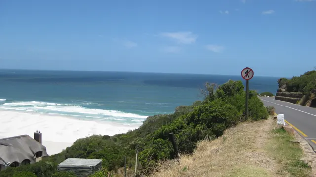 A roadside verge overlooks blue water and white surf along the coast.
