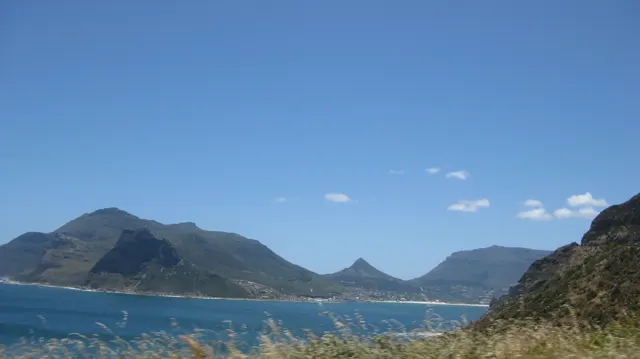 Dry foreground grasses frame a blue bay enclosed by mountainous headlands.