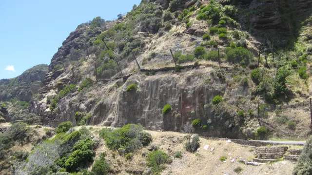 A reinforced road cuts horizontally across a steep green and rocky mountainside.
