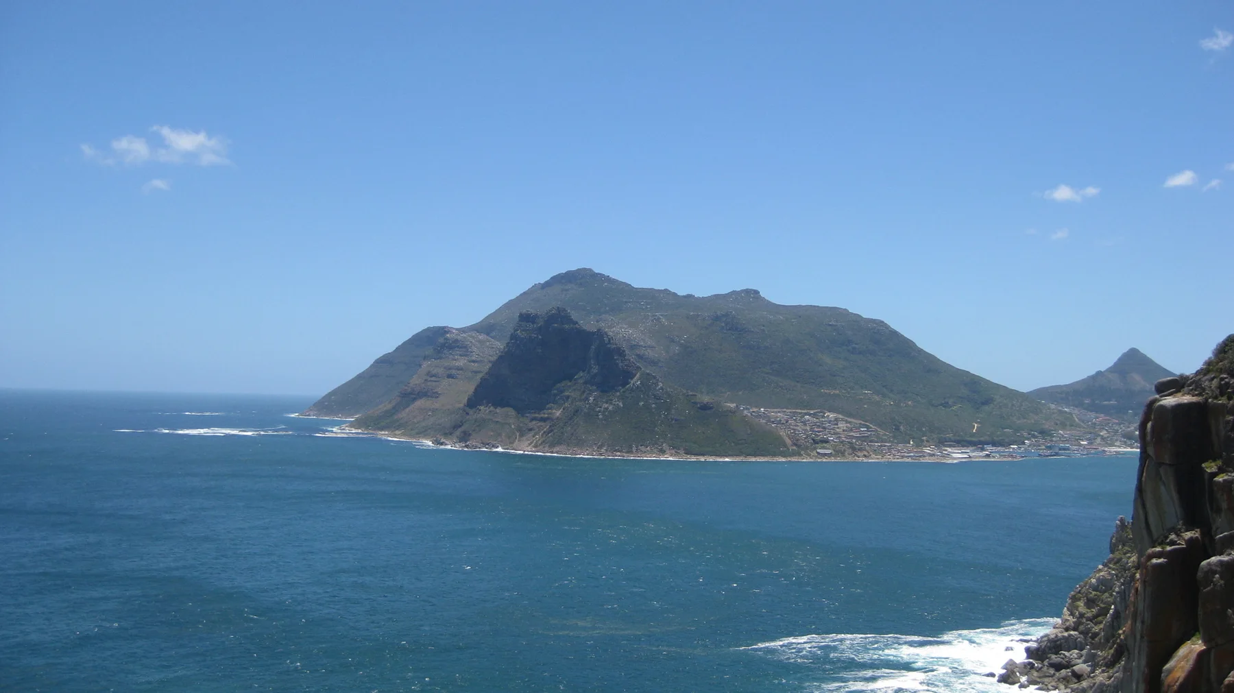 Deep blue water stretches toward a steep headland on the opposite shore.