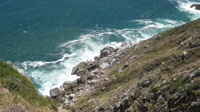 White waves curl around rocks beneath a steep coastal slope.