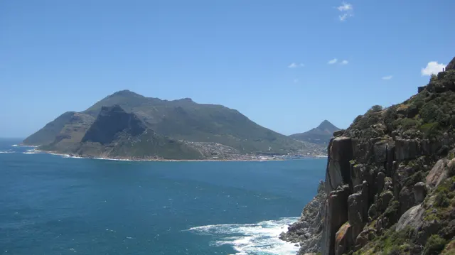 Blue water fills a bay between a distant headland and a dark foreground cliff.