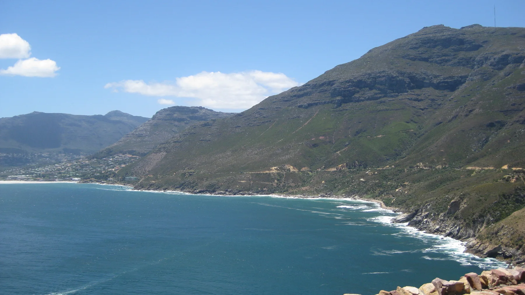 A blue bay curves beneath mountains and a green slope on the right.