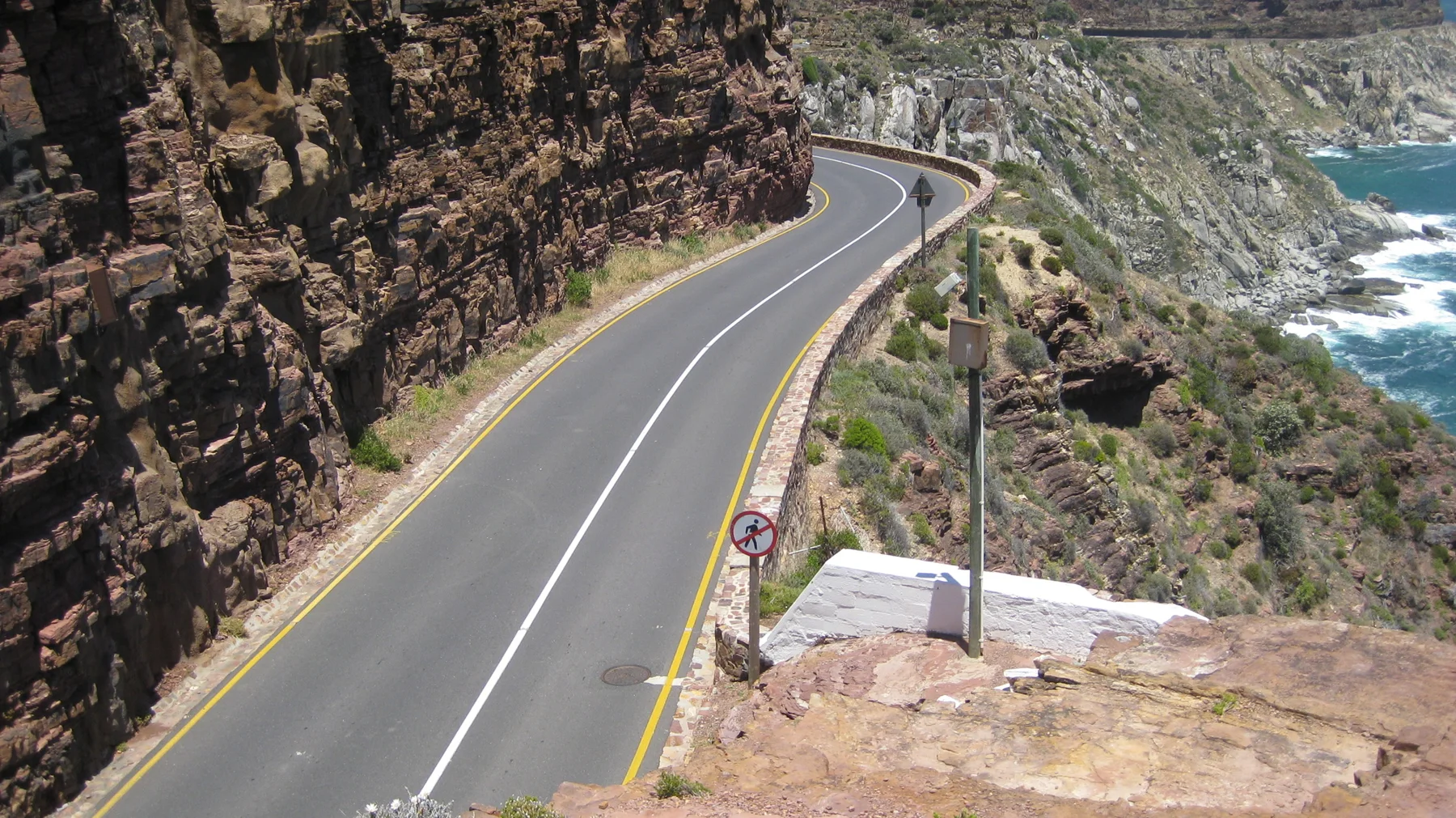 A winding coastal road runs between dark rock faces and white surf far below.