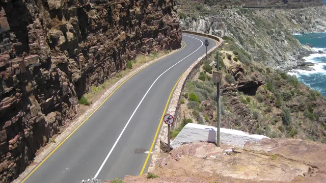 A winding coastal road runs between dark rock faces and white surf far below.